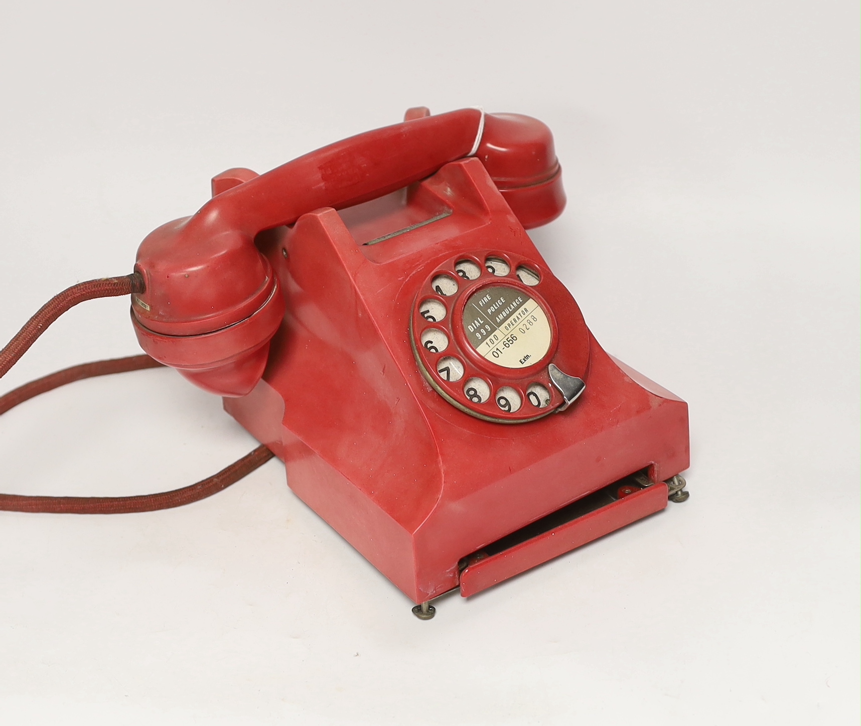 A red 1950s Ericsson Telephones Ltd telephone made in the pattern of a GPO 332 series bakelite telephone, serial no.N1002A 23T, understood to be intended for issue in a tropical country
